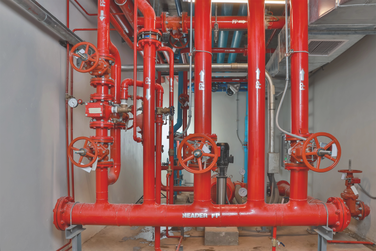 Red fire sprinkler riser pipes and alarm valves in a commercial mechanical room